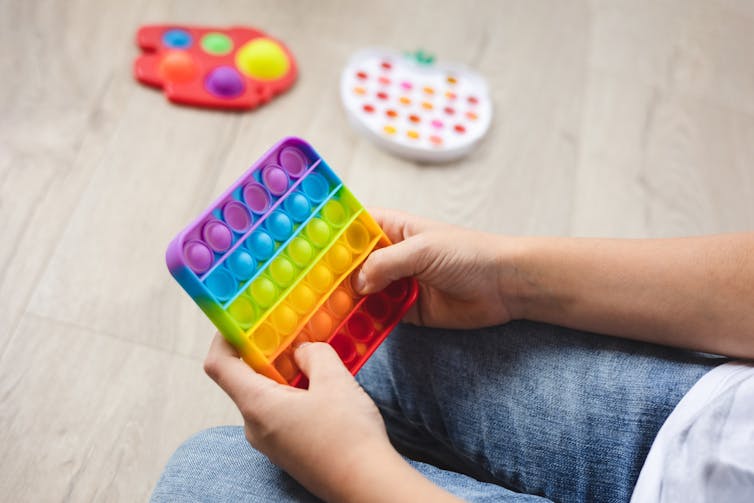 Cropped image of a pop-it toy in a child's hands, and two other toys in the background.