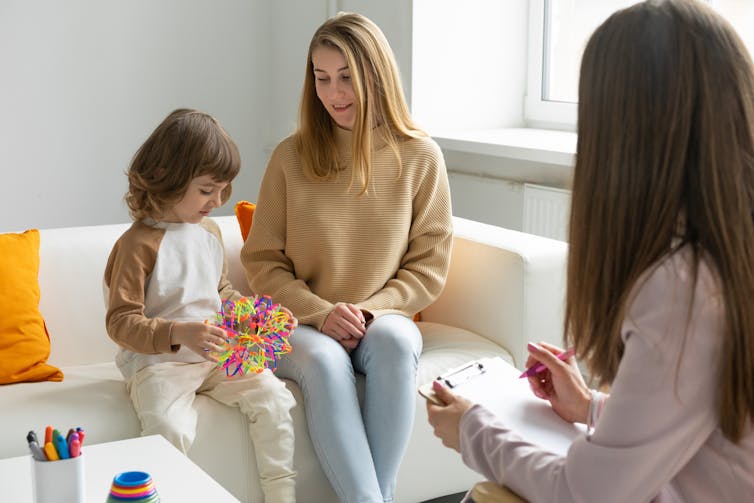 A woman and child on a sofa in a therapist's office, with a therapist seen from behind