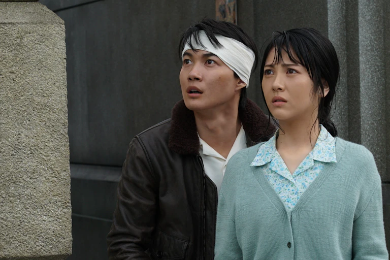 Two people seen looking with fear upwards, one person with a bandage on his head.