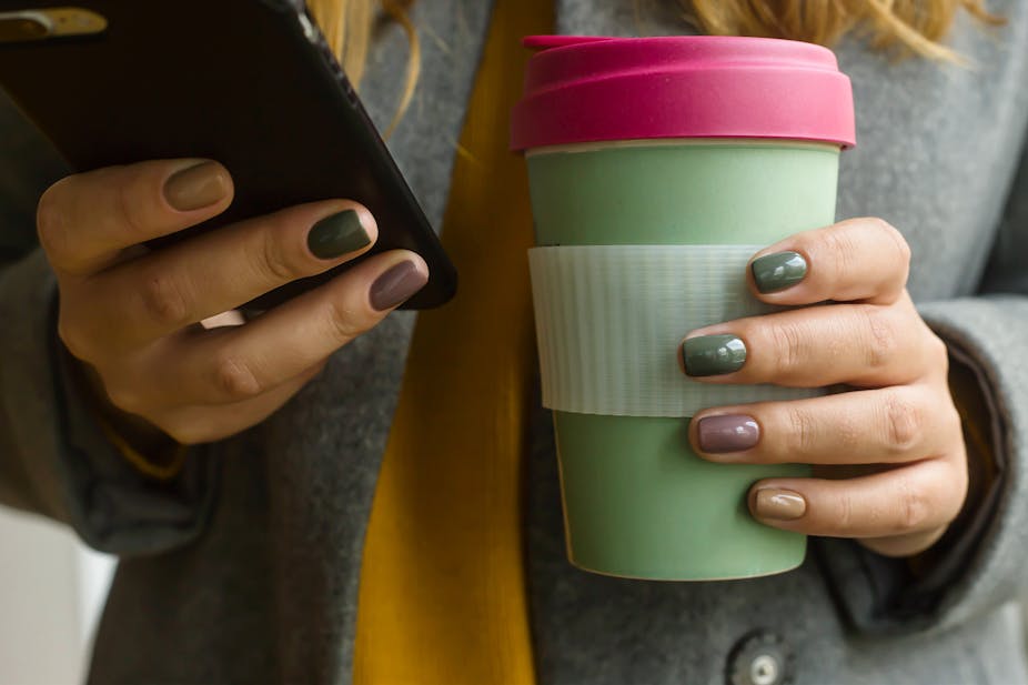 Woman holding a phone and a keep cup.