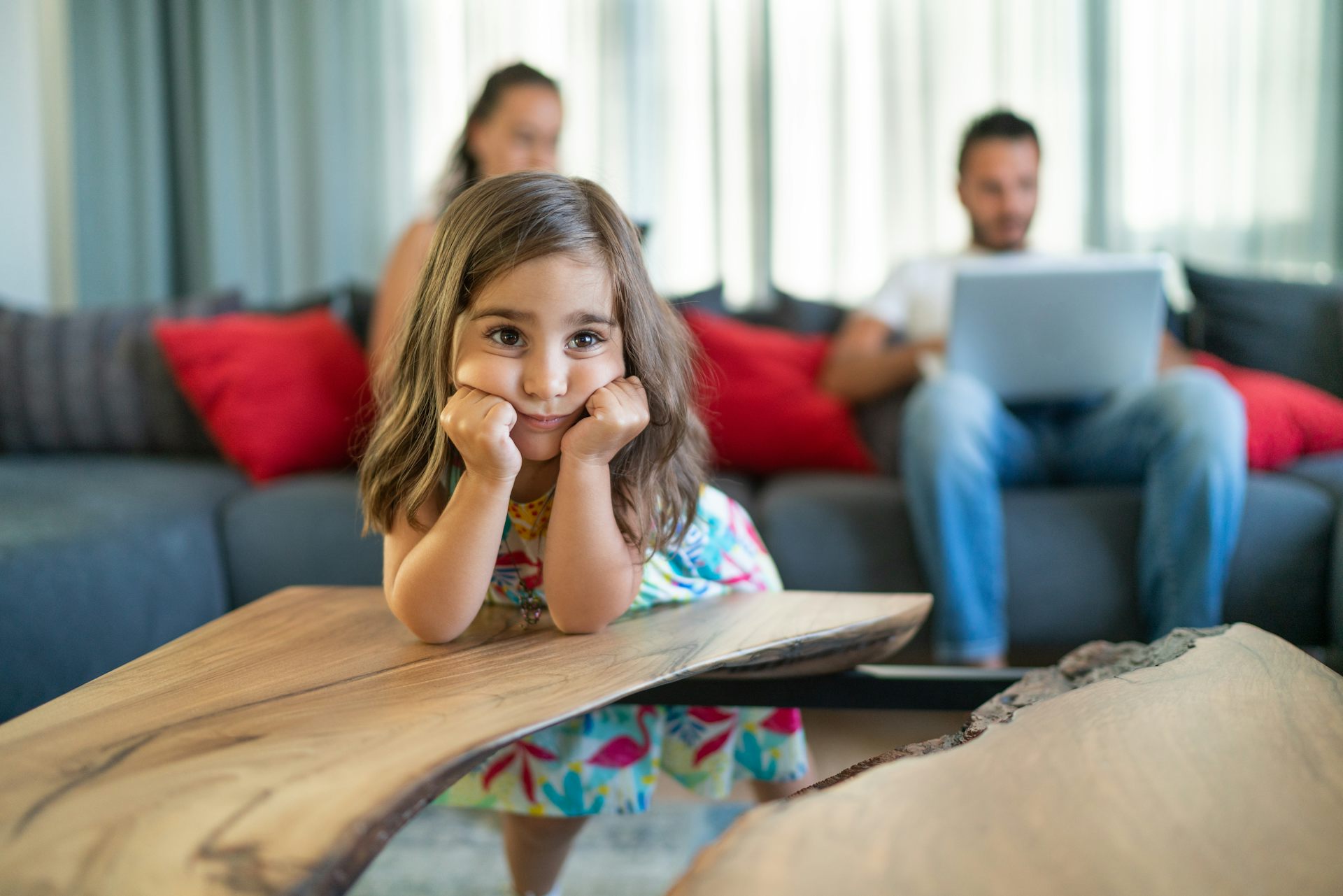 Mother and father using laptop on couch with bored daughter in foreground.