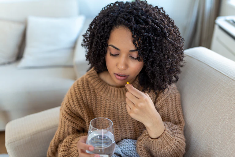 young woman sits on couch and takes capsule