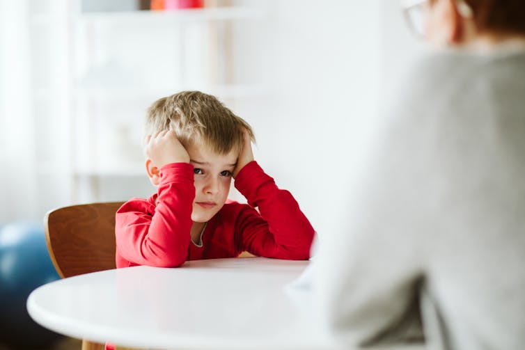 boy looks frustrated, sitting at table with adult