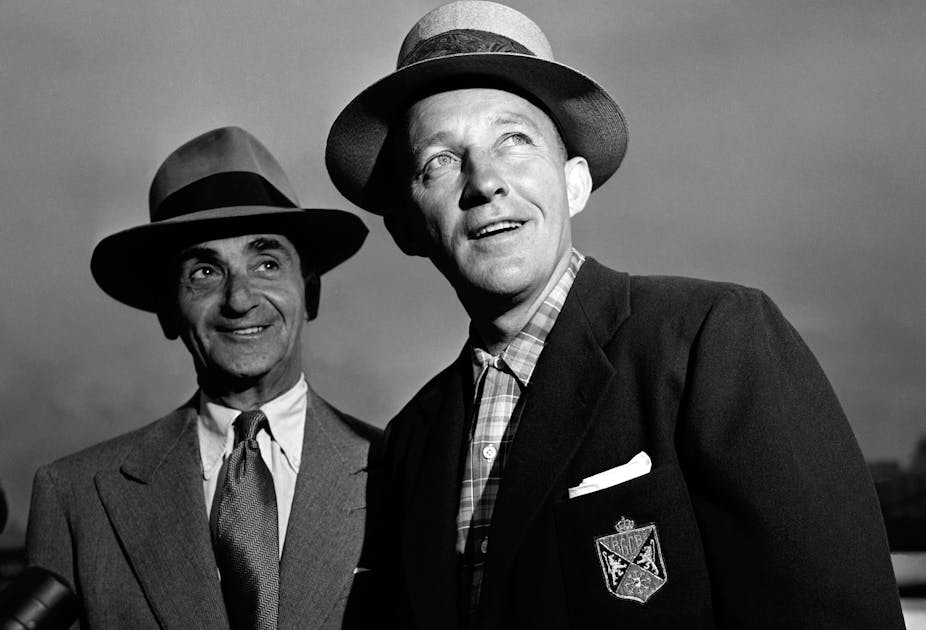 Vintage photo of two men smiling and looking askance wearing hats and suit jackets.