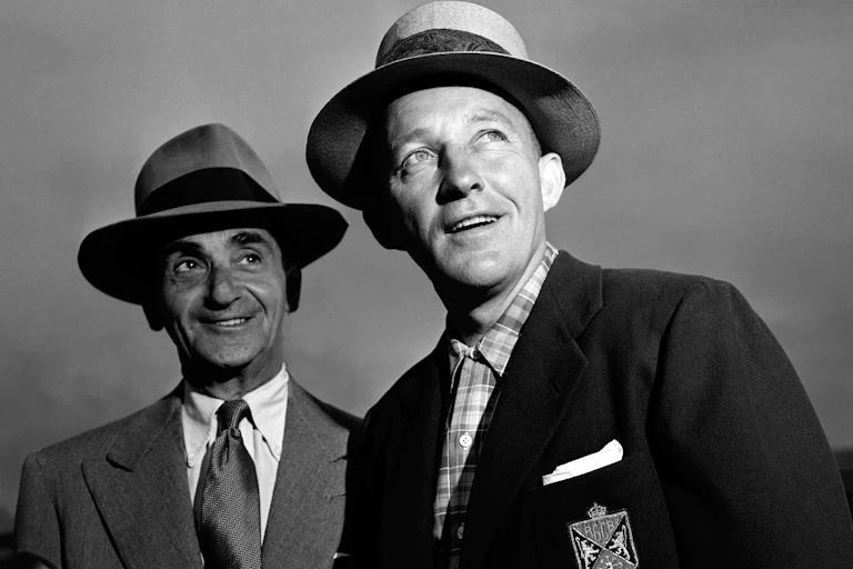 Vintage photo of two men smiling and looking askance wearing hats and suit jackets.