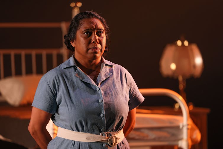 Production image: a woman stands on stage.