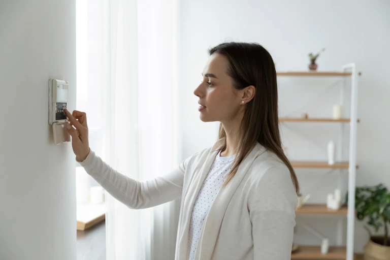 A woman faces her air con control panel and switches it on.
