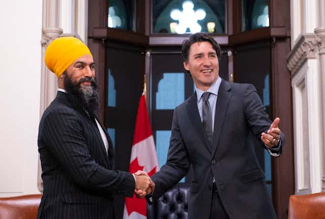 Two men, one in a yellow turban, smile as they shake hands.  A Canadian flag is behind them.