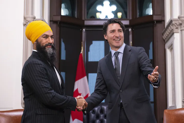 Two men, one in a yellow turban, smile as they shake hands. A Canadian flag is behind them.
