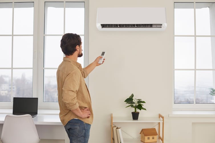 A man points his AC remote at the AC unit on the wall.