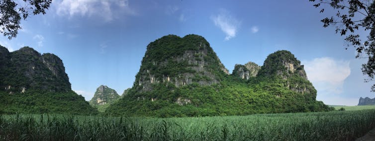 A series of flat-topped tall cliffs covered in greenery set against a blue sky