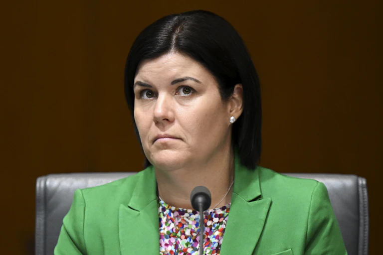 A woman in a bright green blazer sits behind a microphone0