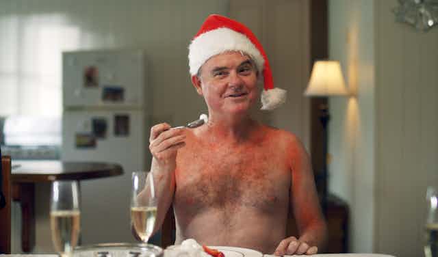 A man, topless and sunburnt, in a Santa hat.