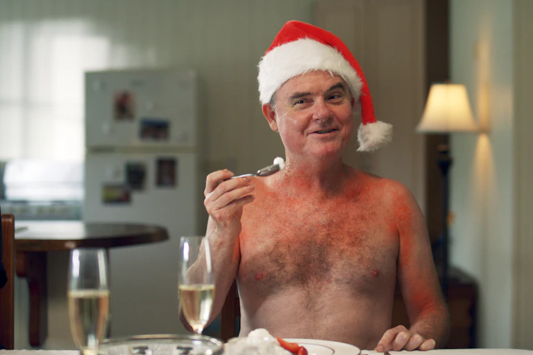 A man, topless and sunburnt, in a Santa hat.