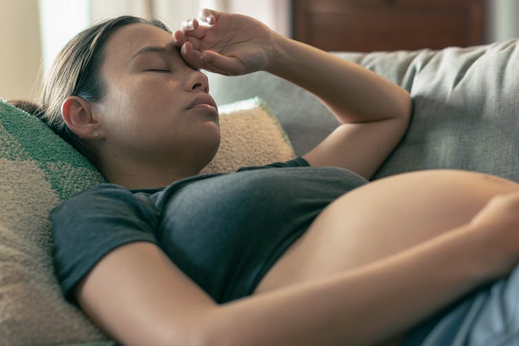 A nauseous pregnant woman lays on a couch.