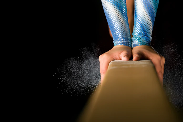 Detailed shot of female gymnast balancing on balance beam with chalk dust on black background