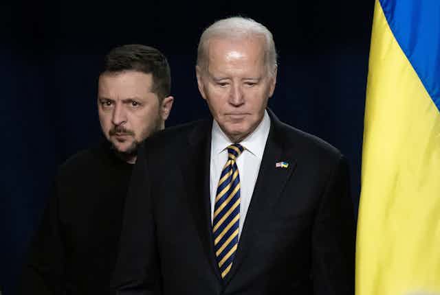 US president Joe Biden next to a Ukrainian flag with Ukrainian president Volodymyr Zelensky behind him.
