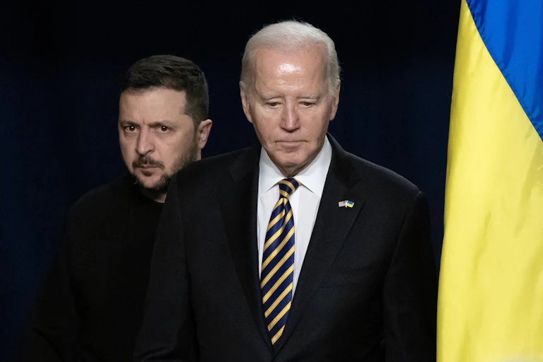 US president Joe Biden next to a Ukrainian flag with Ukrainian president Volodymyr Zelensky behind him.