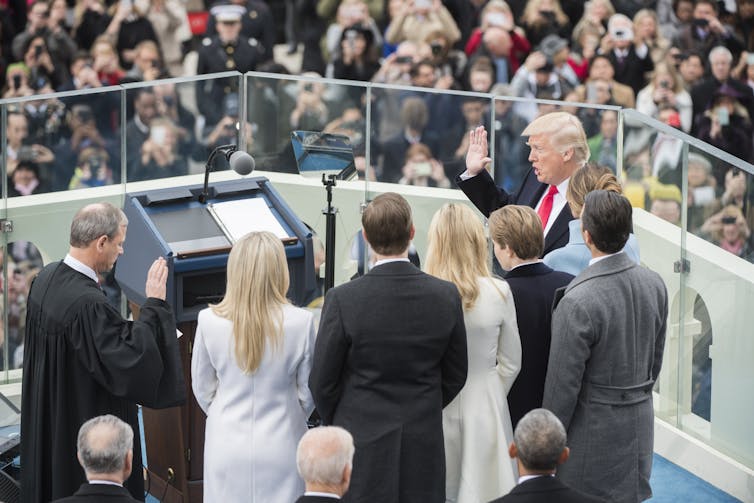 A man in a suit raises his right hand and takes an oath, administered by a man in a judicial robe.