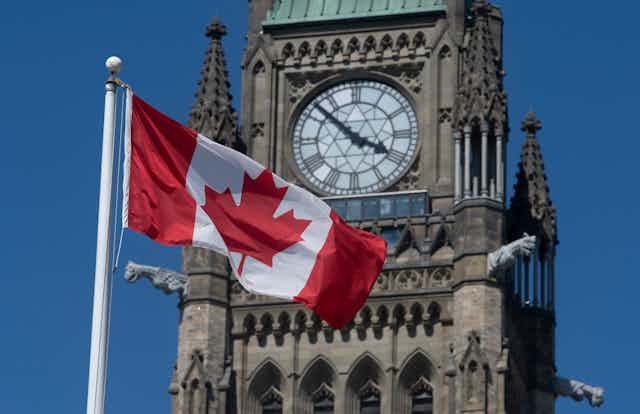 A Canadian flag flies in front of a clock tower