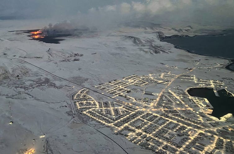 An aerial photo shows the lights of Grindavík and glow of the eruption very nearby.