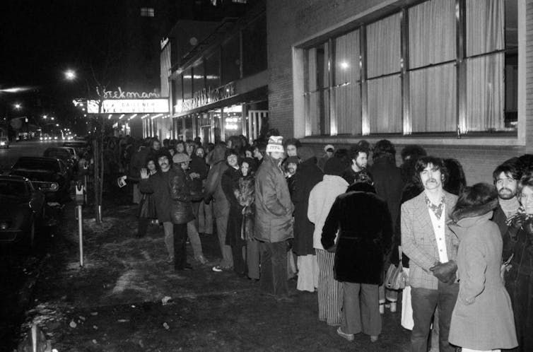 Black and white photo of bundled up people lined up outside of a movie theater.
