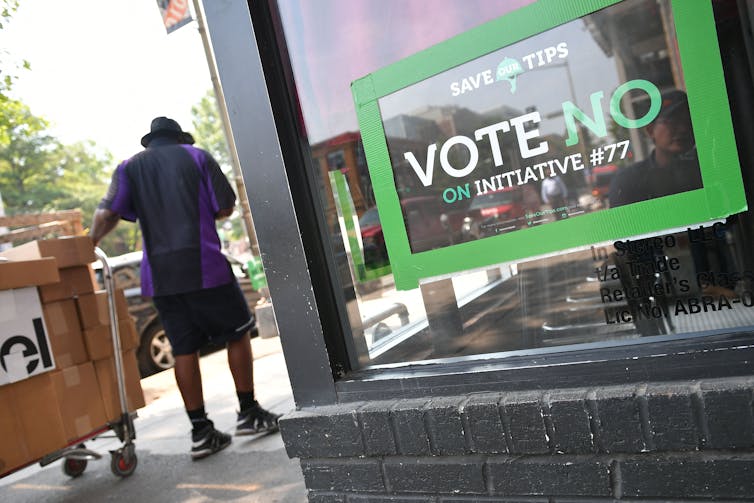 A green-bordered sign on a window that says 'VOTE NO on Initiative #77.'