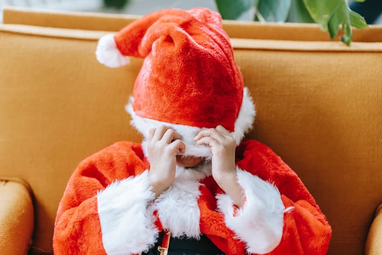 A child in a Santa suit pulls the hat over their head.
