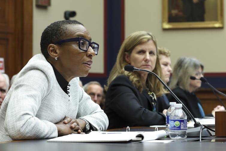 Two women in professional attire speak into microphones.