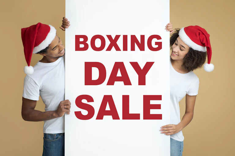 Man and woman wearing Santa hats holding up a "Boxing Day Sale" sign
