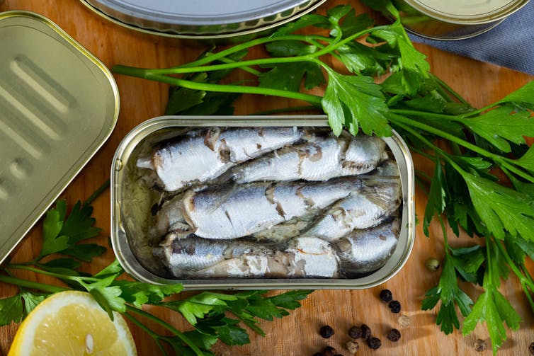 Open sardine can, parsley, cut lemon on wooden table.