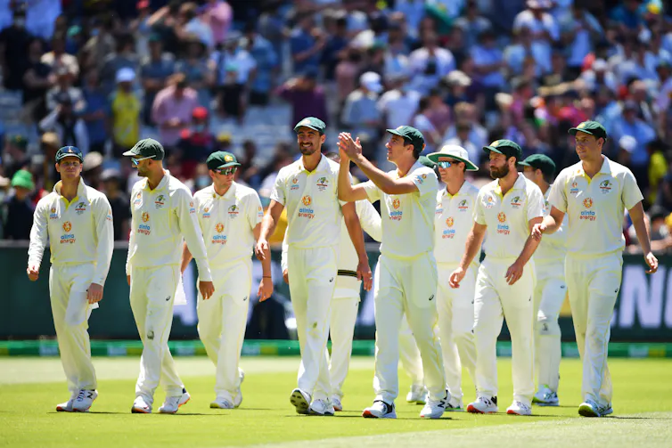 A team of cricketers walking off the cricket pitch at the end of a game