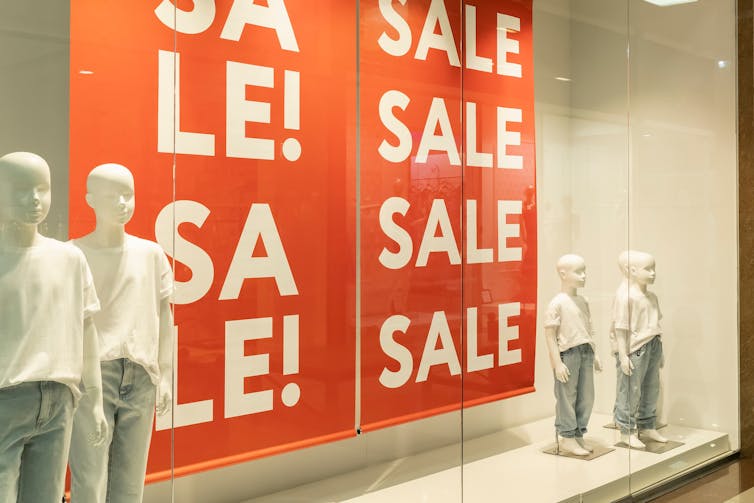 Mannequins standing either side of a Sale banner in a shop window