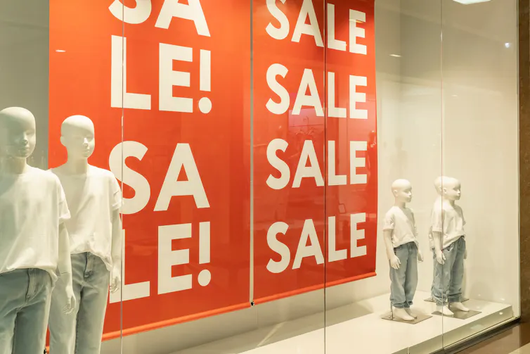 Mannequins standing either side of a Sale banner in a shop window