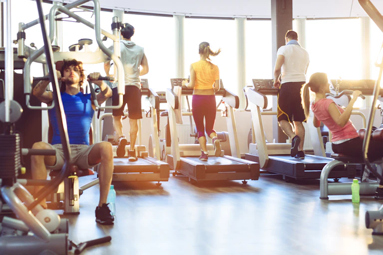 people on treadmills and using weight machines at a gym