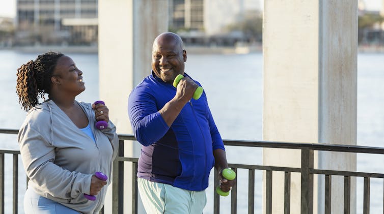 smiling woman and man walking outdoors with hand weights