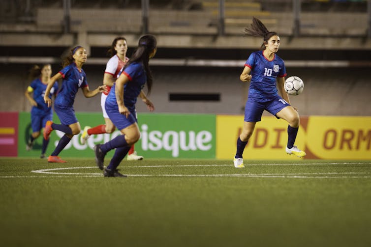 Female soccer players chase the ball.