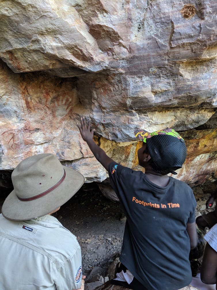 Two people touching a wall with rock art showing outlines of human hands