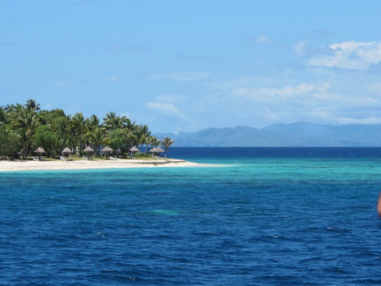 A Fijian island surrounded by blue ocean and blue sky.