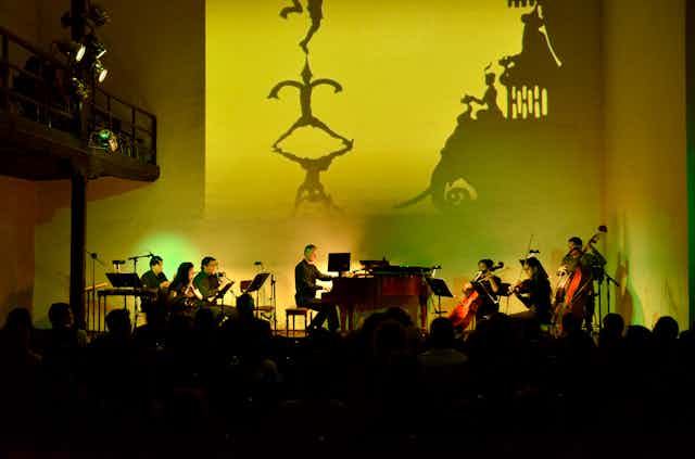 Un conjunto musical toca ante una pantalla en la que se proyecta una película.