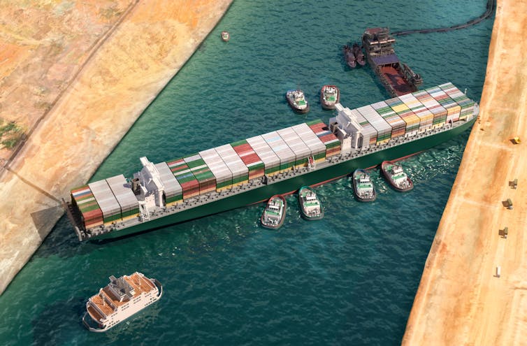 Large container ship stuck at an angle in a canal, surrounded by smaller ships.