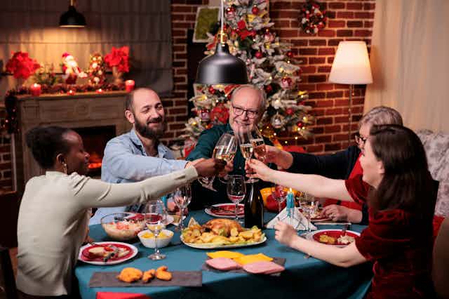 A group of friends and family clink glasses over Christmas dinner.