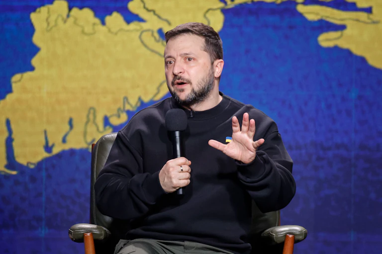 Ukrainian president Volodymyr Zelensky talks into a microphone while sitting in front of a map of Ukraine.