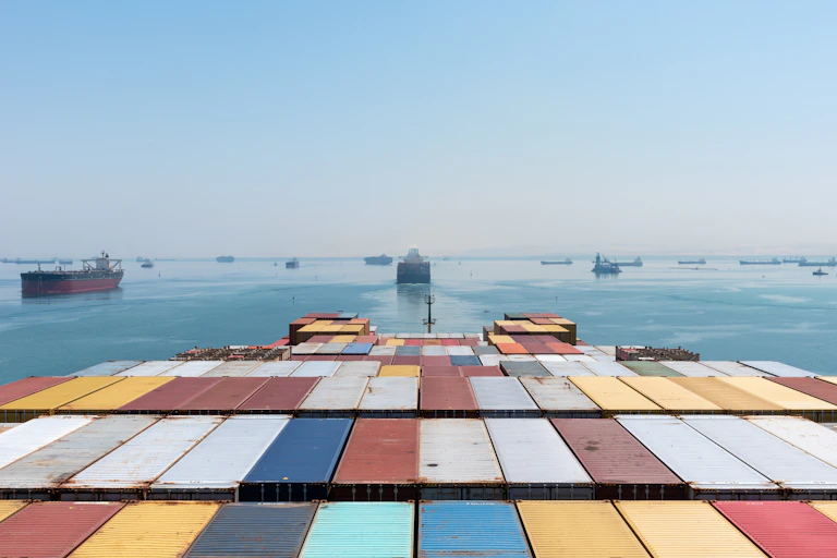 Containers loaded on deck of cargo ship, with other ships in the background.