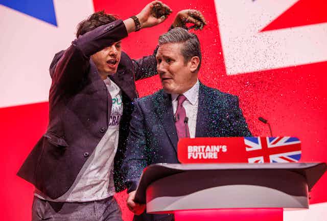 A protester throws glitter over Labour leader Keir Starmer as he stands at the podium at Labour Party conference