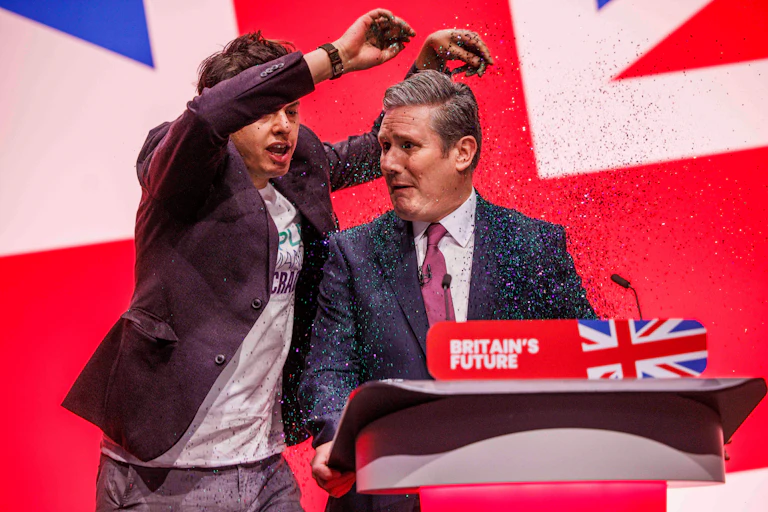 A protester throws glitter over Labour leader Keir Starmer as he stands at the podium at Labour Party conference