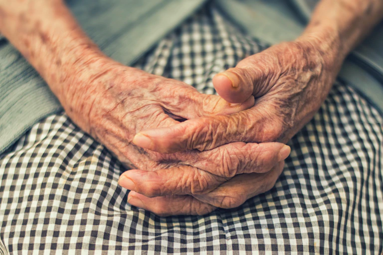 An old lady's hands against a checkered skirt.