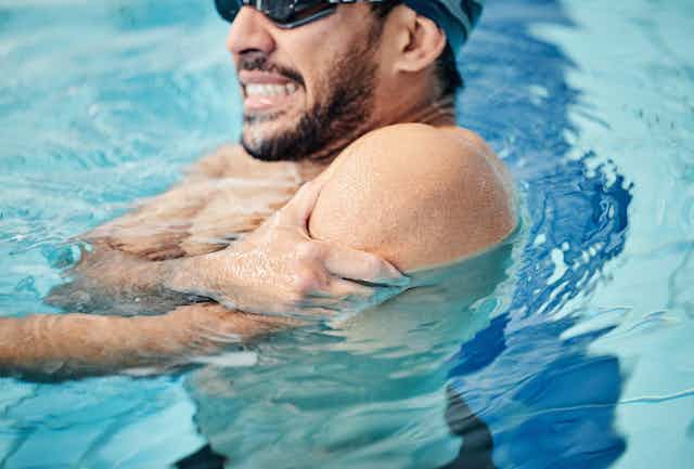Man in a swimming pool gripping his shoulder
