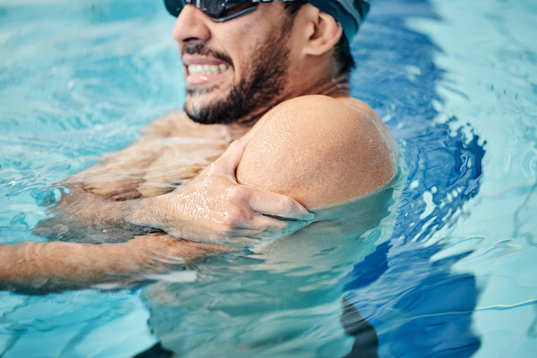 Man in a swimming pool gripping his shoulder