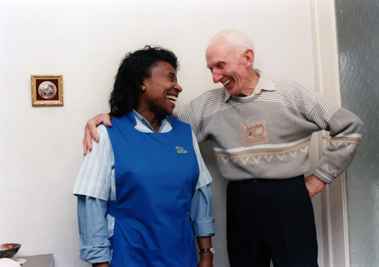 A care workers in a blue apron with an elderly man.